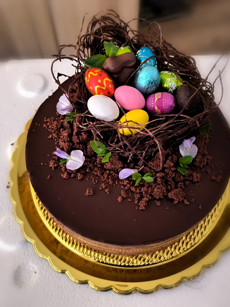 Torta glassata al cioccolato con nido di cioccolato, ovetti pasquali e fiori eduli