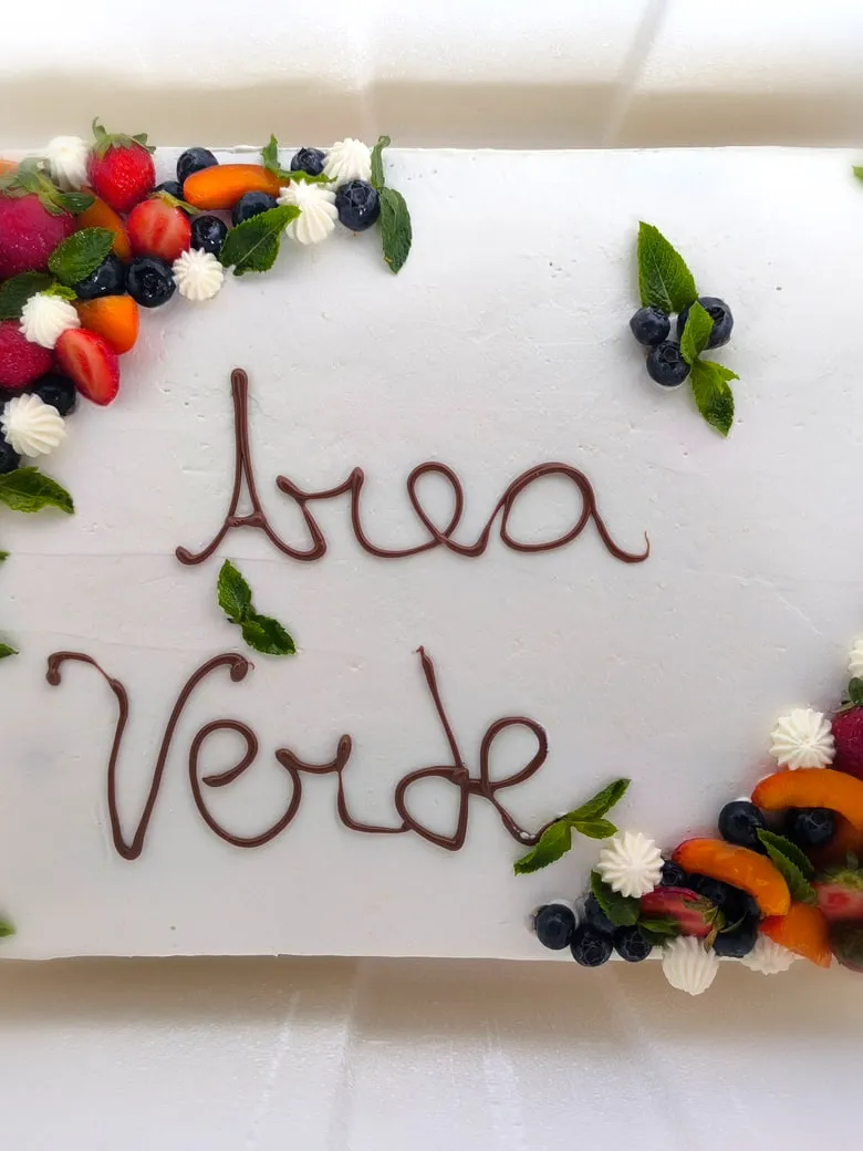 Torta rettangolare glassata di bianco con scritta al cioccolato e cornice di frutti di bosco