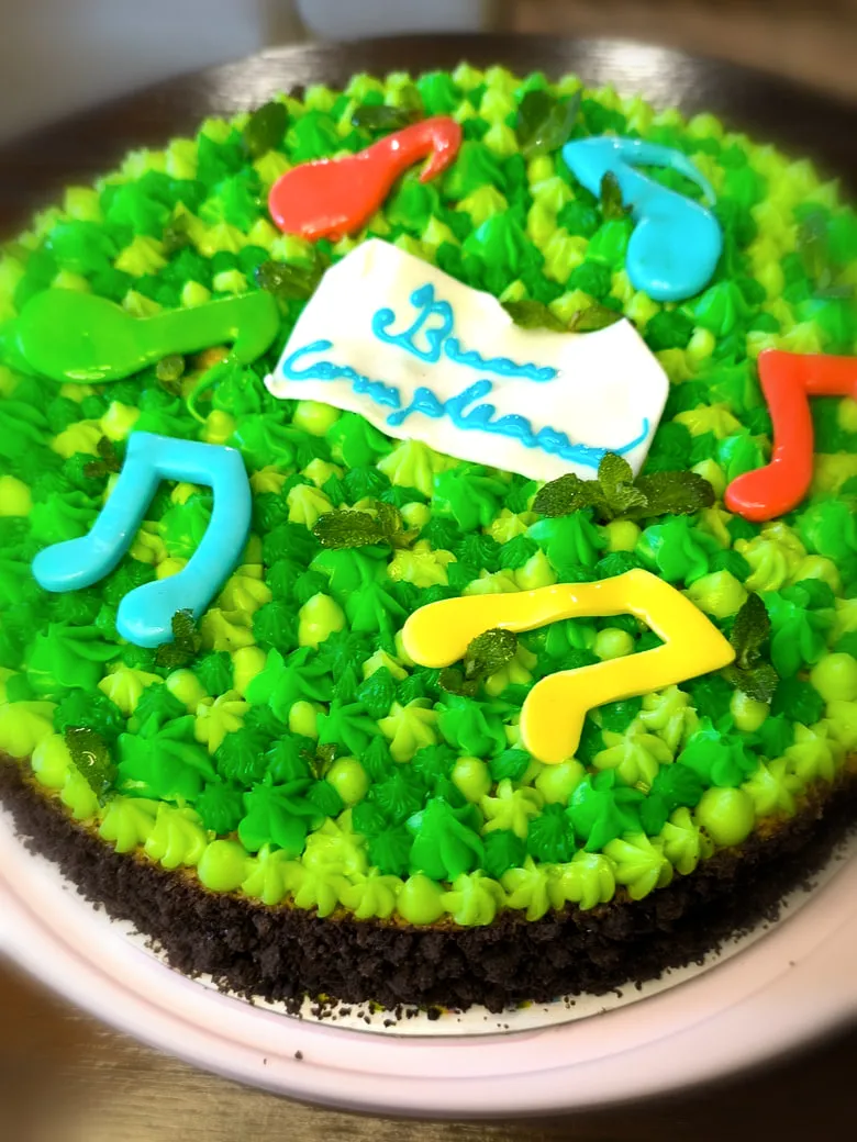 Torta di compleanno decorata a ciuffi verdi con note musicali colorate