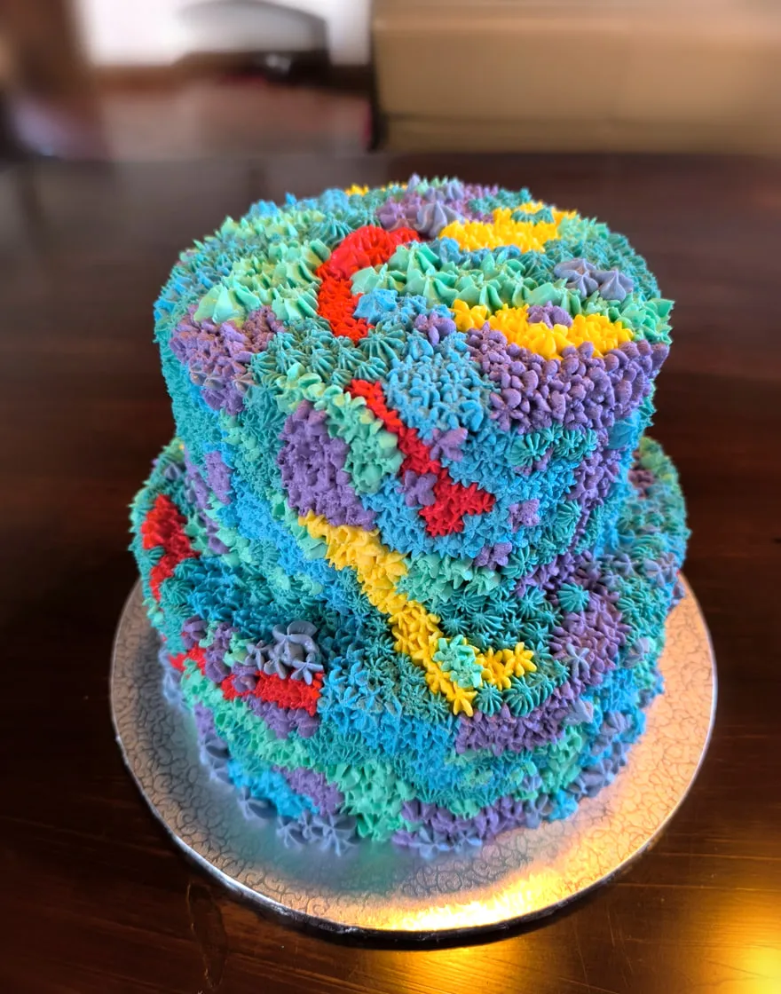 Torta a due piani interamente decorata a mano con ciuffi di crema turchese, viola, gialla e rossa