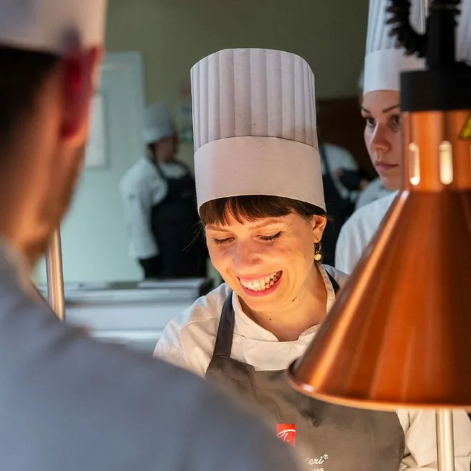 Martina Lucarini sorride mentre lavora in una cucina professionale, con il cappello da chef